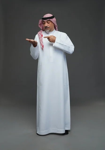 رجل سعودي بالثوب التقليدي يشير لراحة يده في الاستوديو
