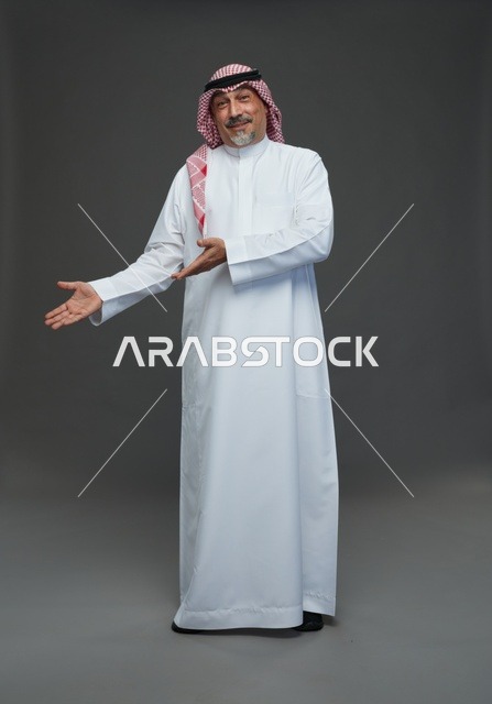 رجل سعودي بالزي التقليدي يشير بيده بخلفية رمادية