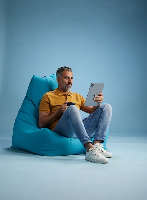 رجل سعودي يسترخي على كرسي بين باج مع جهاز لوحي وقهوة