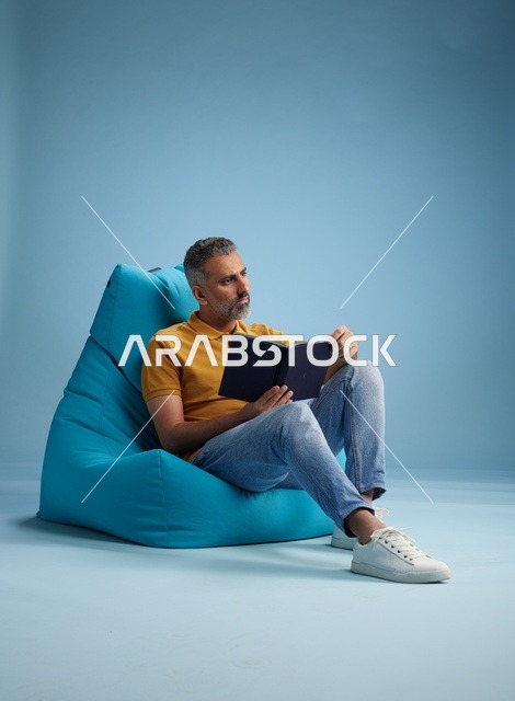 رجل سعودي يقرأ كتاباً على مقعد استرخاء داخل استوديو