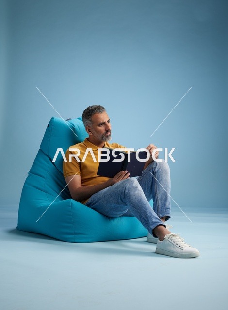 رجل سعودي يقرأ كتاباً على مقعد مريح في الاستوديو