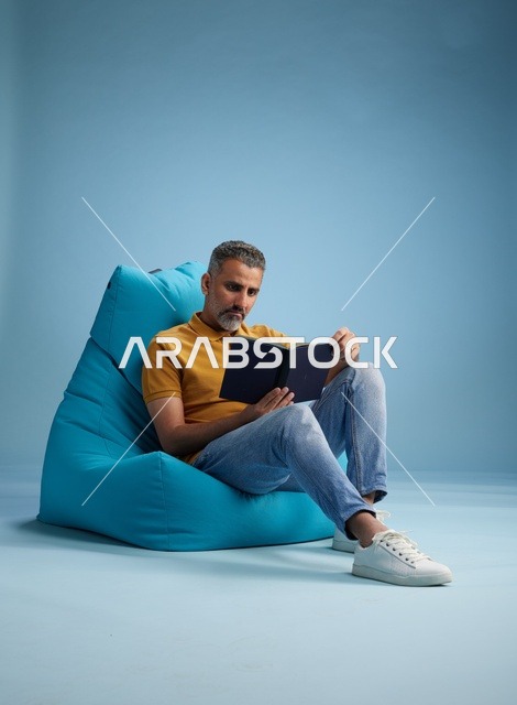 رجل سعودي يقرأ كتاباً على مقعد محشو أزرق