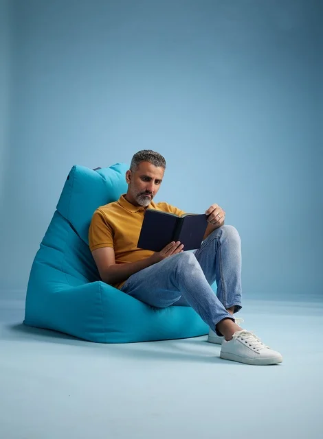 رجل سعودي يقرأ كتاباً على مقعد محشو أزرق