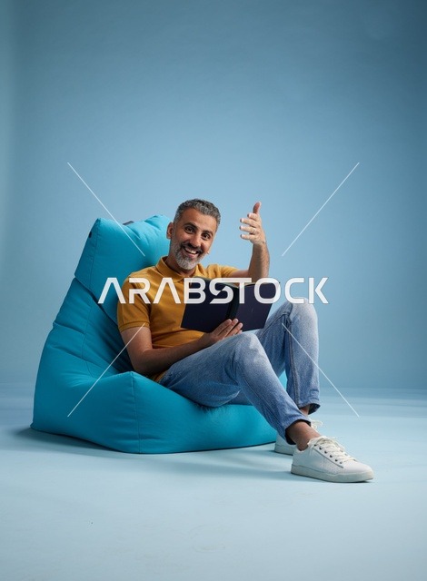 Middle Aged Saudi Man Reading Book on Blue Beanbag