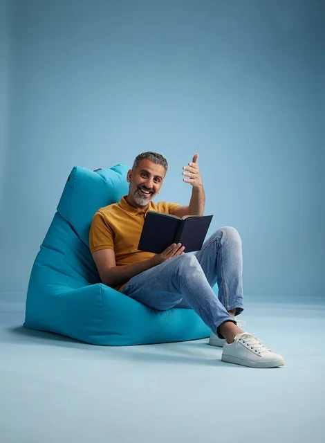 Middle Aged Saudi Man Reading Book on Blue Beanbag