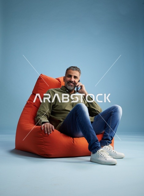 رجل سعودي يتحدث بالهاتف جالس على بين باج برتقالي