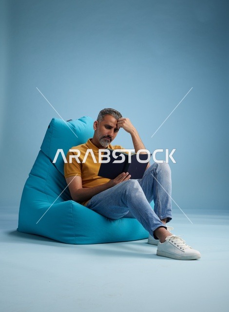 رجل سعودي يقرأ كتاباً على مقعد محشو أزرق
