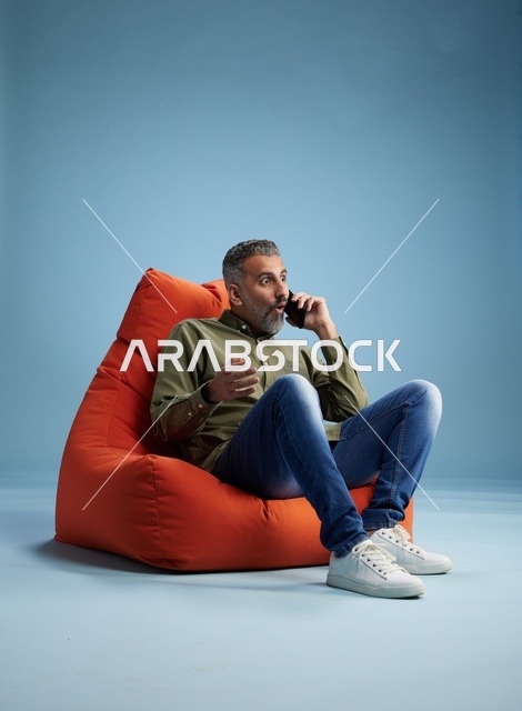 رجل سعودي يتحدث عبر الهاتف على مقعد برتقالي