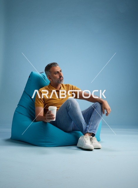 رجل سعودي يسترخي على كرسي بين باج مع كوب قهوة