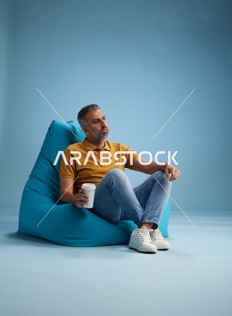 رجل سعودي يسترخي على كرسي بين باج مع كوب قهوة