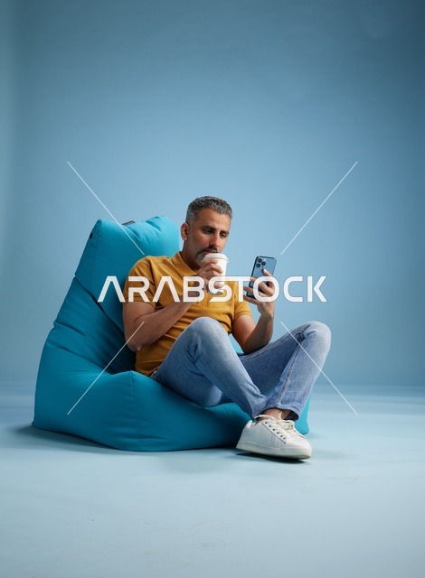 رجل سعودي يسترخي على مقعد مع كوب قهوة وهاتف