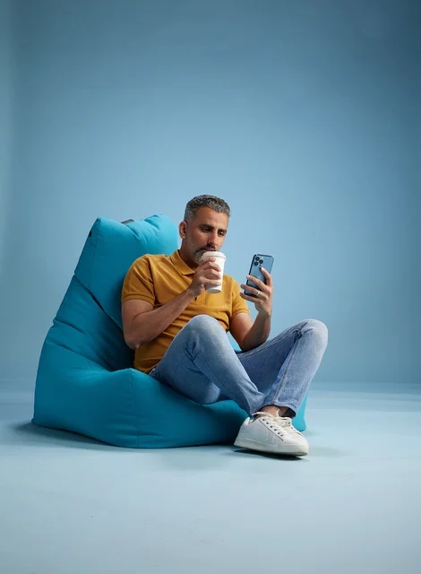 رجل سعودي يسترخي على مقعد مع كوب قهوة وهاتف