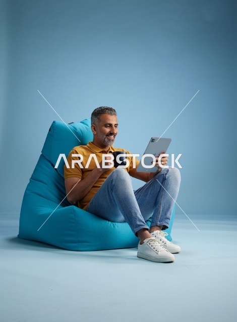 رجل سعودي يسترخي على كرسي بين باج مع جهاز لوحي