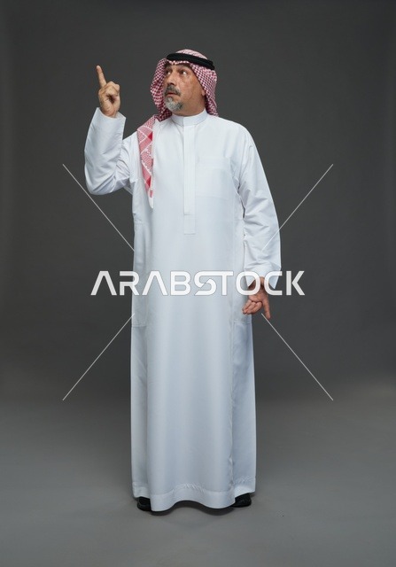 رجل سعودي بالزي التقليدي يشير للأعلى في الاستوديو