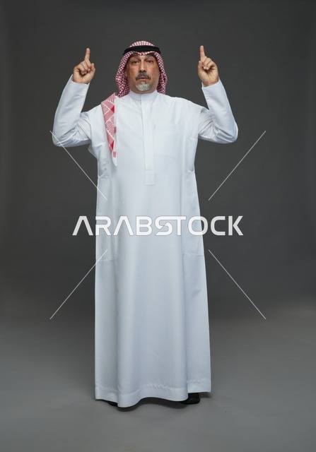 رجل سعودي بالزي التقليدي يشير للأعلى بخلفية رمادية