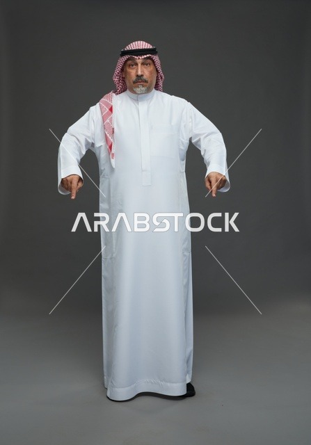 رجل سعودي بالزي التقليدي يشير للأسفل في استوديو