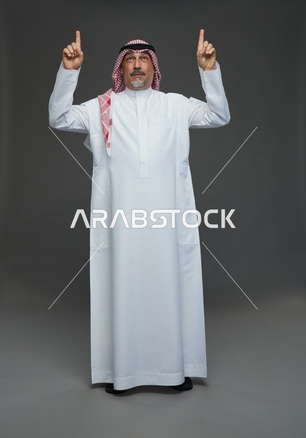 رجل سعودي بالزي التقليدي يشير للأعلى خلفية رمادية
