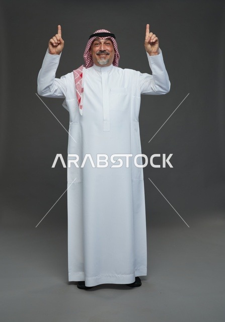 رجل سعودي بالزي التقليدي يشير للأعلى في استوديو
