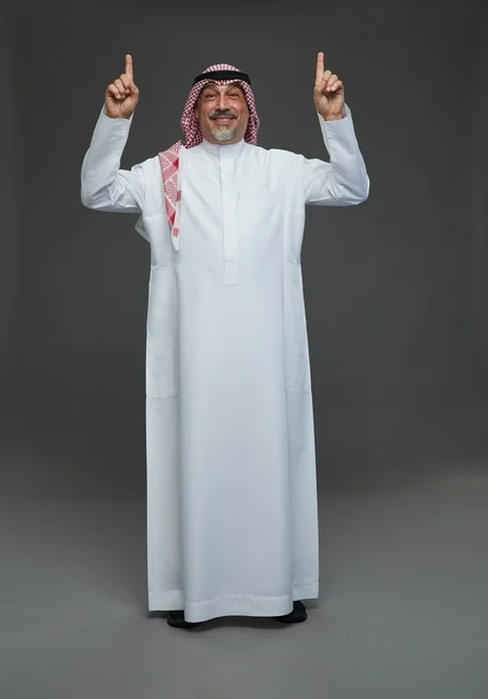 رجل سعودي بالزي التقليدي يشير للأعلى في استوديو