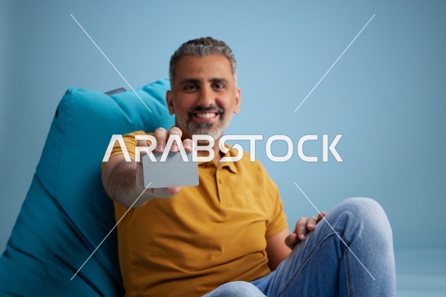 رجل سعودي يحمل بطاقة ائتمان على كرسي بين باق