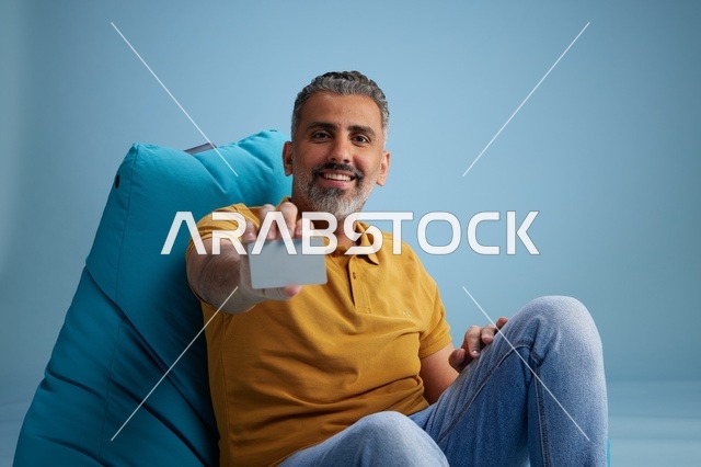 رجل سعودي يحمل بطاقة ائتمان على كرسي بين باج
