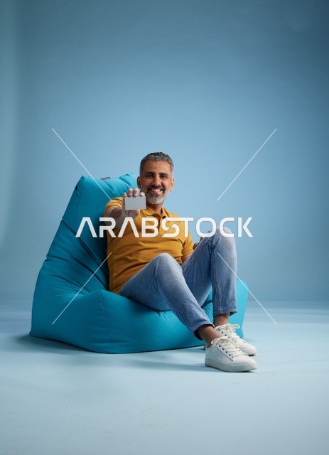 رجل سعودي يحمل بطاقة ائتمان على كرسي بين باج