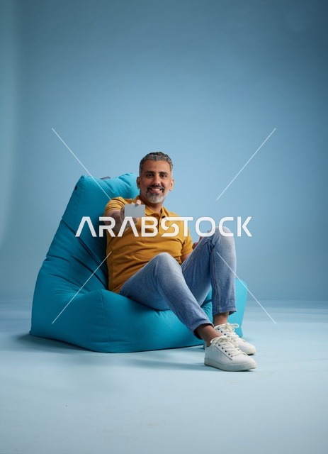 رجل سعودي يحمل بطاقة ائتمان على كرسي بين باق