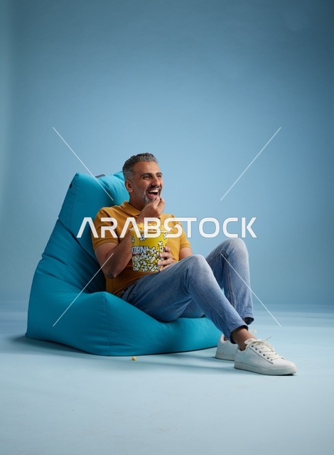 رجل سعودي يأكل الفشار على كرسي بين باج أزرق