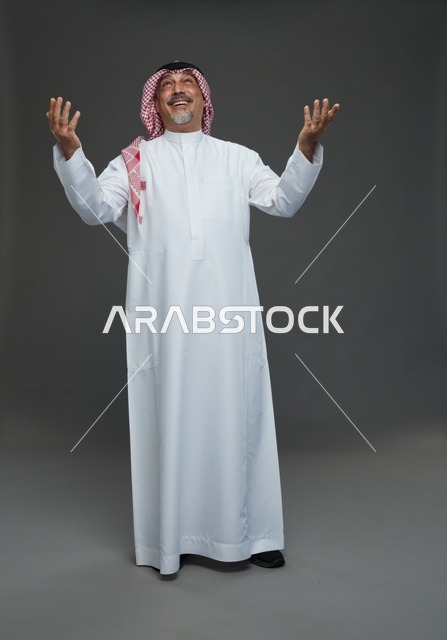 رجل سعودي بالزي التقليدي يرفع يديه للأعلى