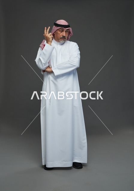رجل سعودي بالزي التقليدي أمام خلفية رمادية