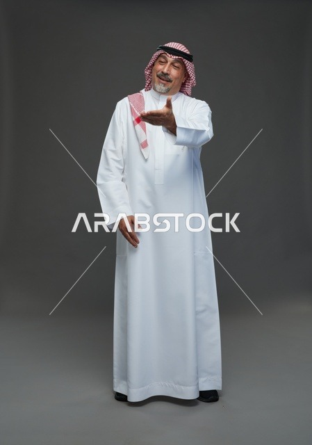 رجل سعودي بالزي التقليدي يشير بيده بخلفية رمادية