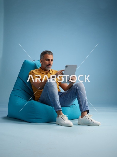 Saudi Man Using Tablet on Blue Bean Bag Chair