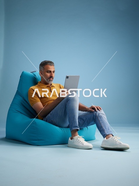 Saudi Man Using Tablet on Blue Bean Bag Chair