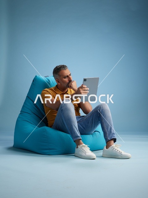 رجل سعودي على كرسي بين باق يستخدم جهاز لوحي