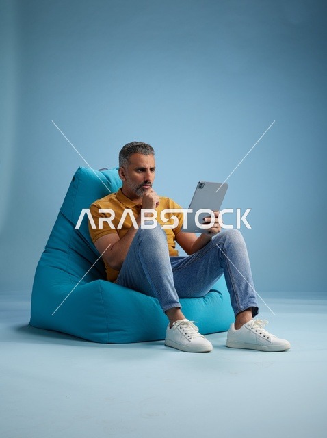 رجل سعودي يستخدم جهاز لوحي جالس على كرسي بين باق