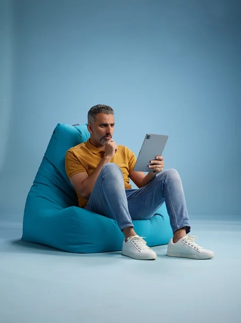 رجل سعودي يستخدم جهاز لوحي جالس على كرسي بين باق