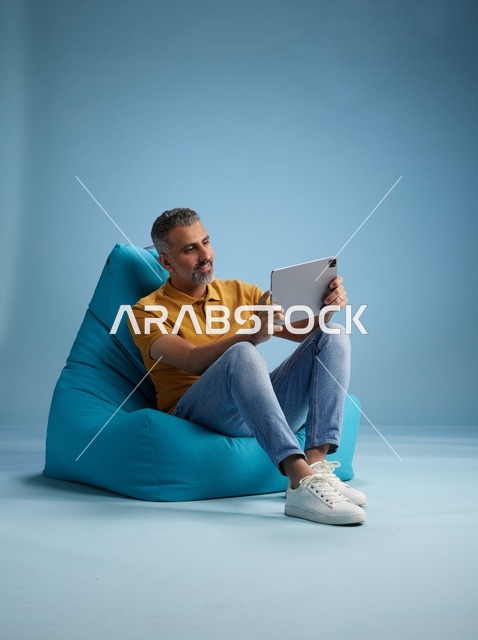 رجل سعودي جالس على كرسي بين باج يستخدم جهاز لوحي