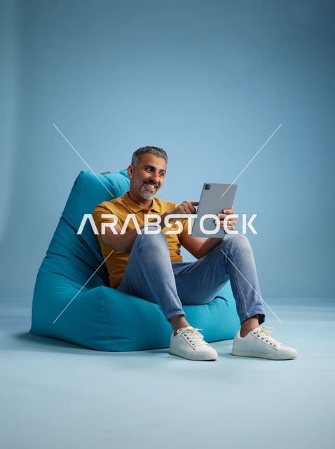 Saudi Man Using Digital Tablet on Blue Bean Bag