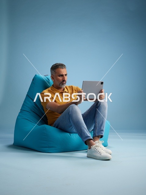 رجل سعودي يستخدم جهازاً لوحياً على كرسي بين باج في استوديو