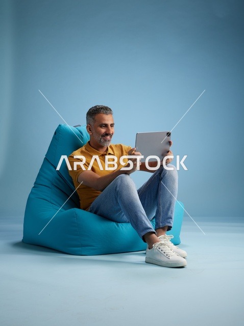 رجل سعودي يستخدم جهاز لوحي على كرسي بين باق