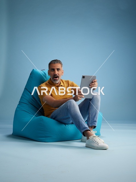 رجل سعودي مندهش مع جهاز لوحي على كرسي بين باج