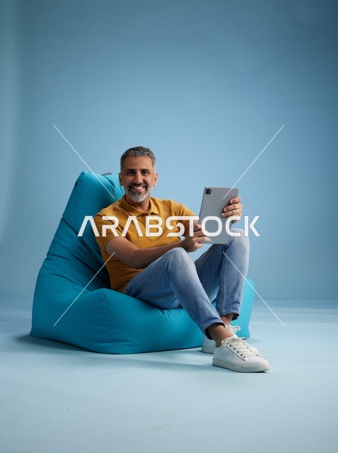 رجل سعودي يجلس على بين باج يستخدم تابلت