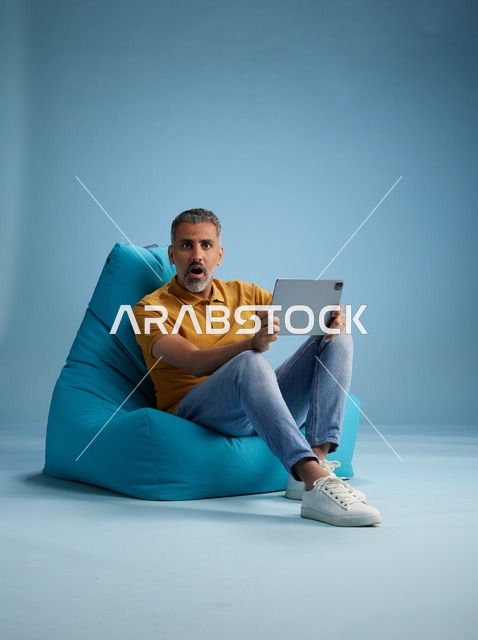رجل سعودي على كرسي بين باق يستخدم جهاز لوحي