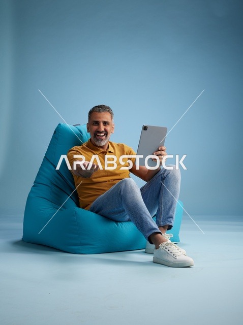 رجل سعودي جالس على كرسي محشو يستخدم جهاز لوحي