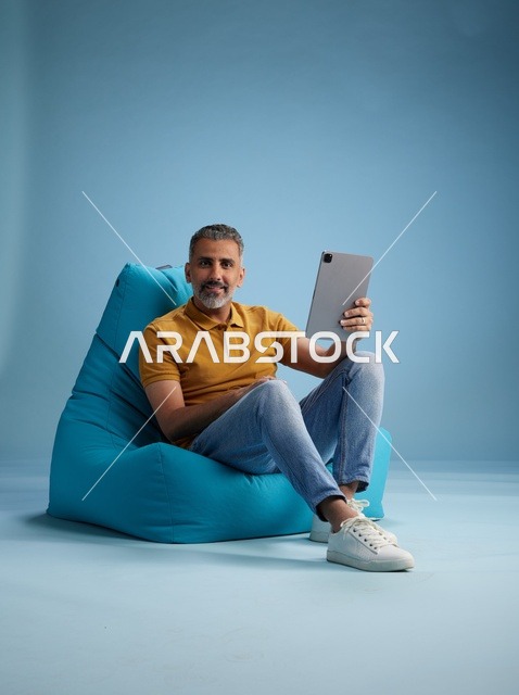 رجل سعودي يستخدم جهاز لوحي على كرسي بين باق