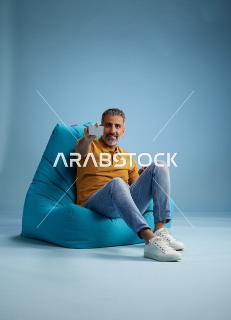 رجل سعودي يحمل بطاقة ائتمان على كرسي بين باج