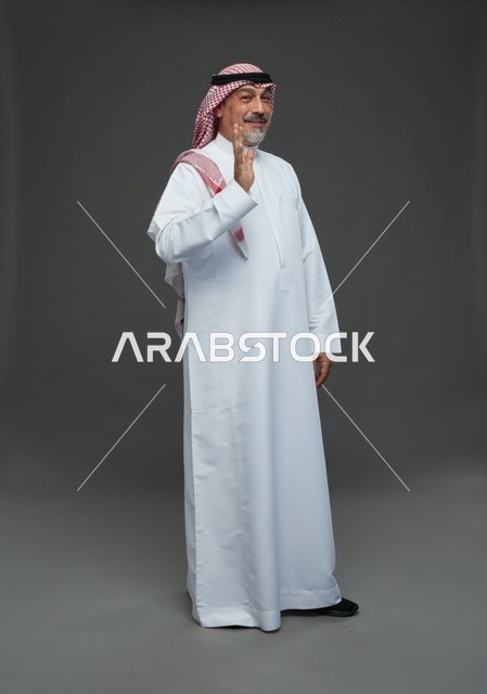 رجل سعودي بالزي التقليدي يلوح بيده بخلفية رمادية