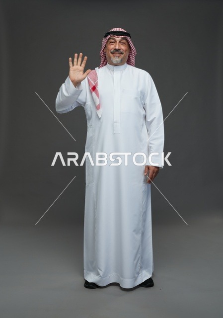 رجل سعودي يرتدي الزي التقليدي يلوح بيده في استوديو
