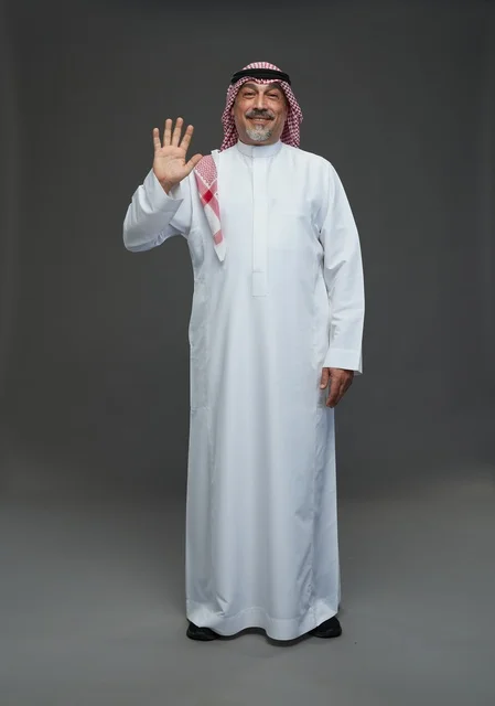 رجل سعودي يرتدي الزي التقليدي يلوح بيده في استوديو