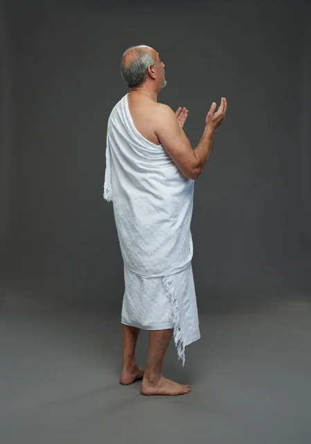 رجل سعودي بملابس الإحرام يدعو بخلفية رمادية